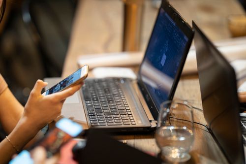 Pessoa usando smartphone e laptop em um ambiente de trabalho interno aconchegante.